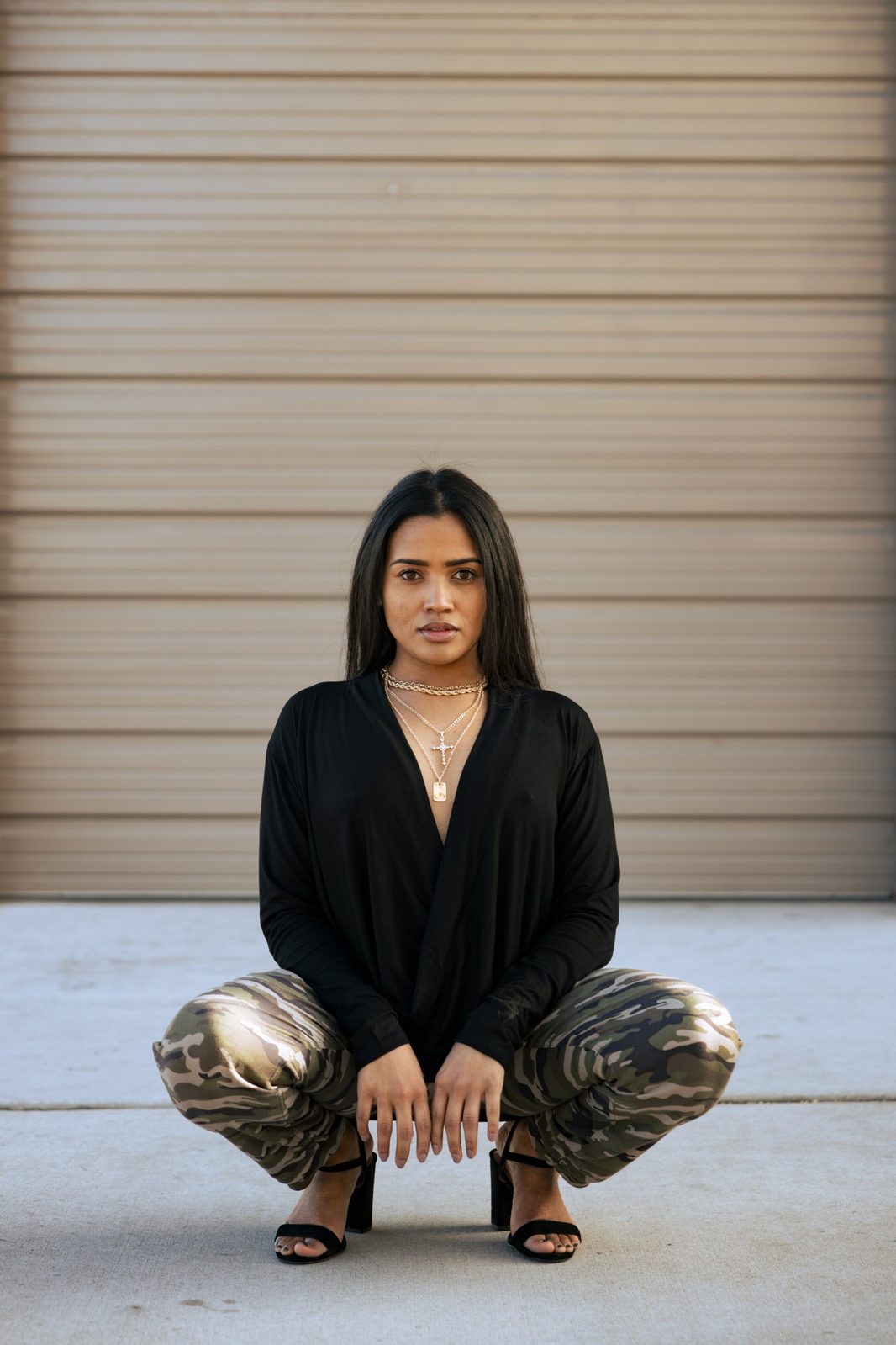 Portrait crouched against a corrugated garage door in camo pants and heels