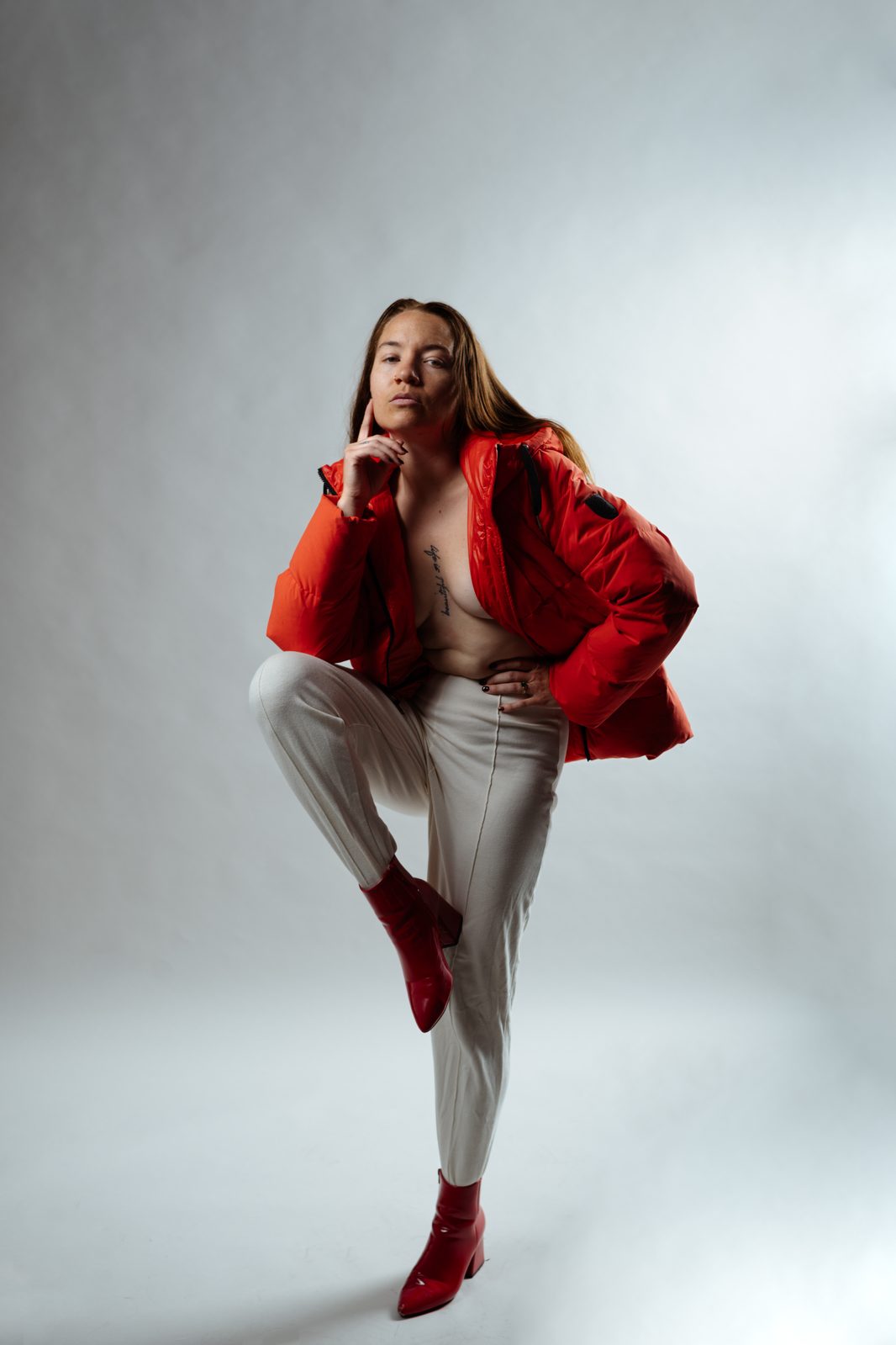Studio editorial portrait in a red puffer jacket and red boots, one knee raised